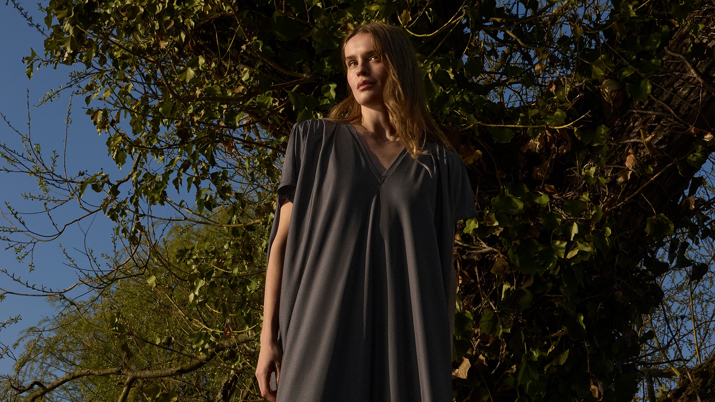 Woman in the INA KESS ETHERA dress in the colour ombre standing in front of trees with a blue sky background.