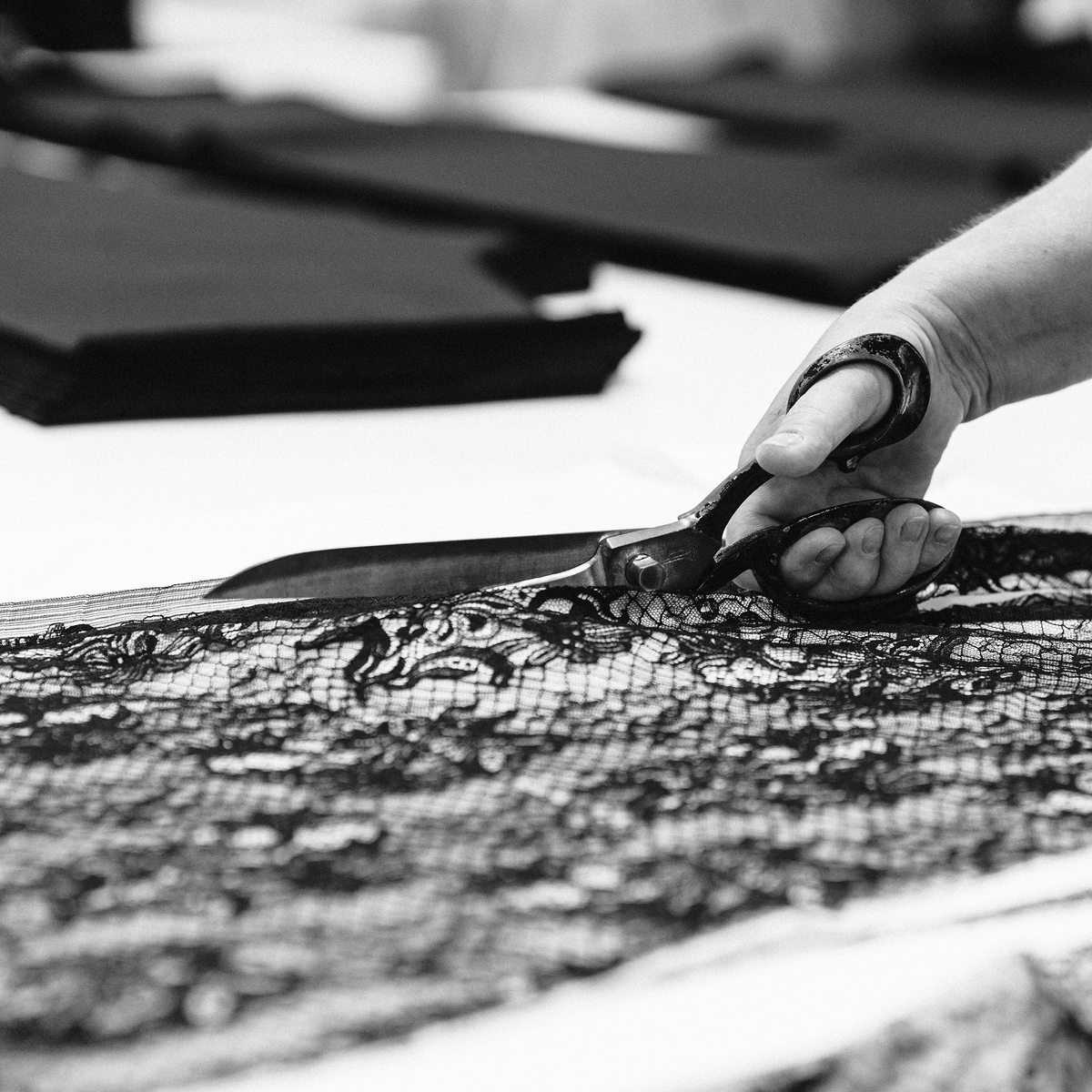 Person cutting black lace fabric with scissors in a workshop setting, which is the INA KESS production in Portugal.